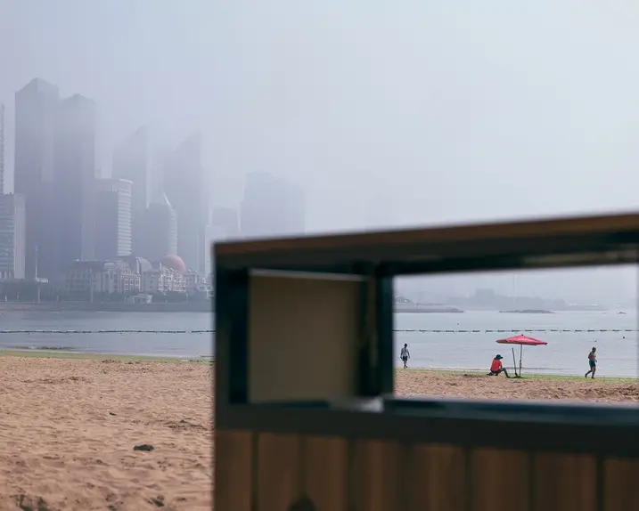 View through the rectangular opening of a garbage can on the beach with skyscrapers in the foggy background.