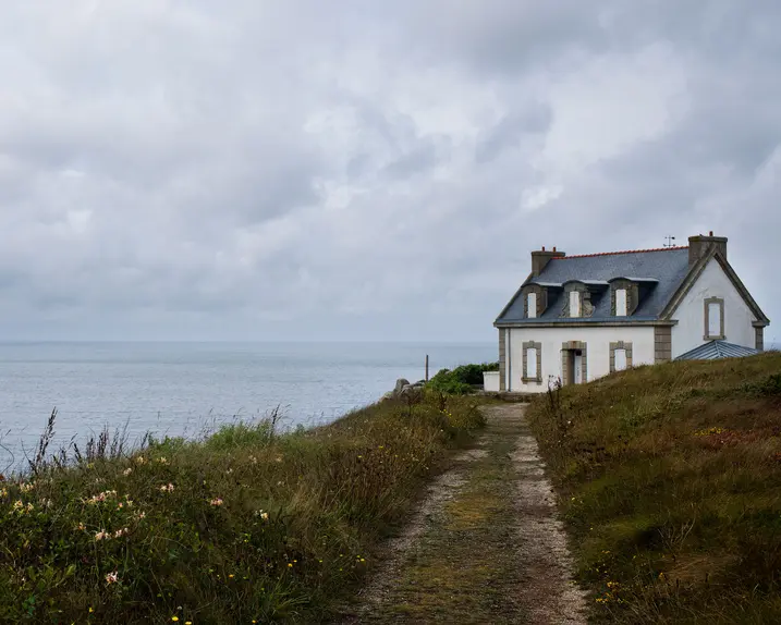 White house on a cliff, surrounded by flowers and a view of the cloudy sea.