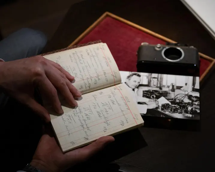Person holding an old paper notebook, a photograph and a camera lie on the table.
