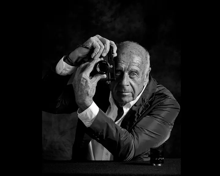 Elderly man holds a camera in front of his face and turns the lens of the camera.