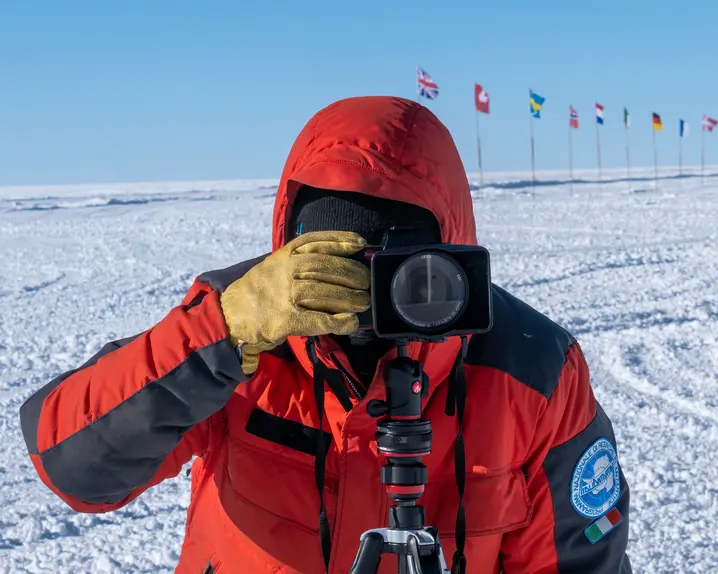 Person takes a photo in a snowy landscape with European flags in the background.
