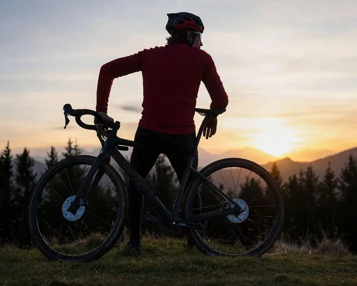 Man leaning on his mountain bike looking at the mountains at sunset.