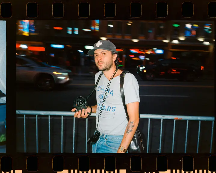 Joe Greer with a Leica M6 in his hand standing at a street at night.