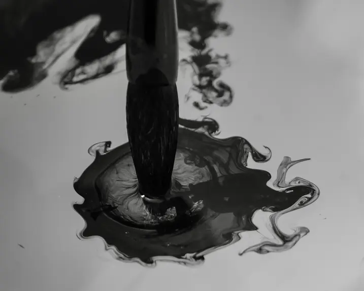 Brush dips into dark ink that spreads in the water.