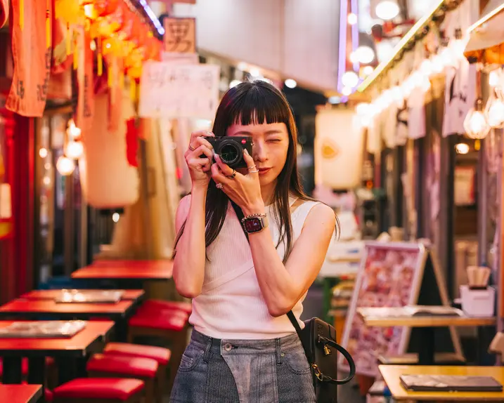 A woman takes pictures with a camera in a colorful, illuminated street.