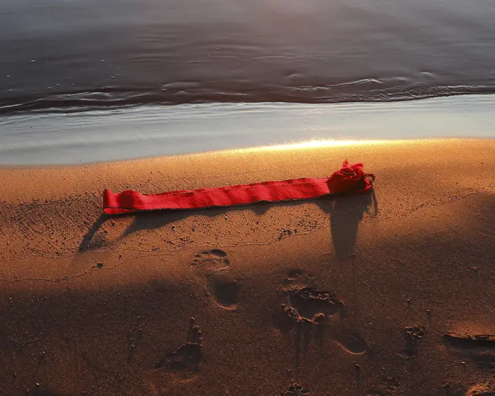 Red ribbon lying on the beach shore at sunset, footprints in the sand.