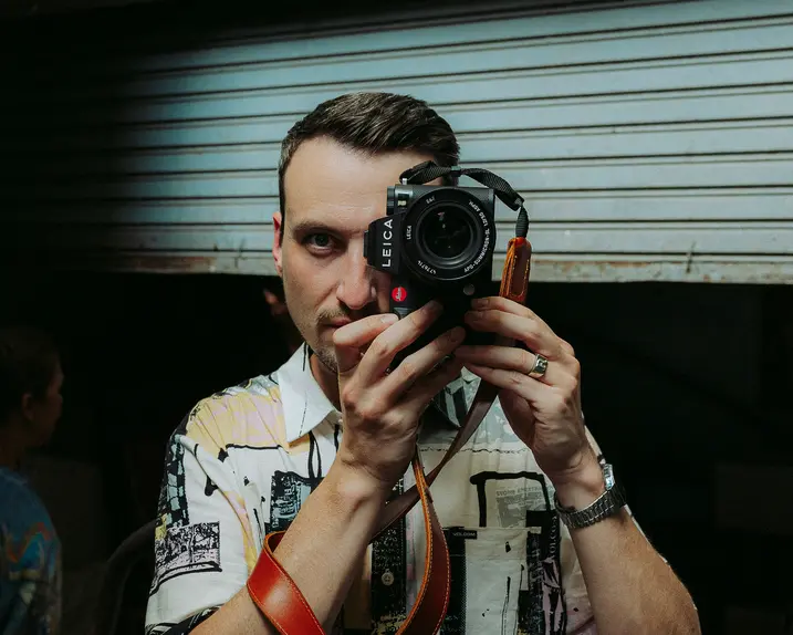 Philipp Reinhard looks through a camera and stands in front of a blue garage door.