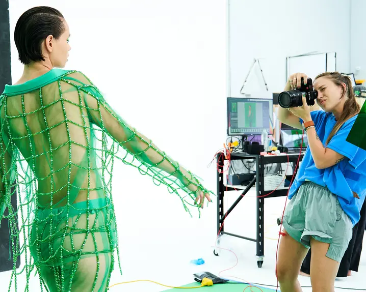 Photographer takes a picture in a studio of a model in a green net outfit.