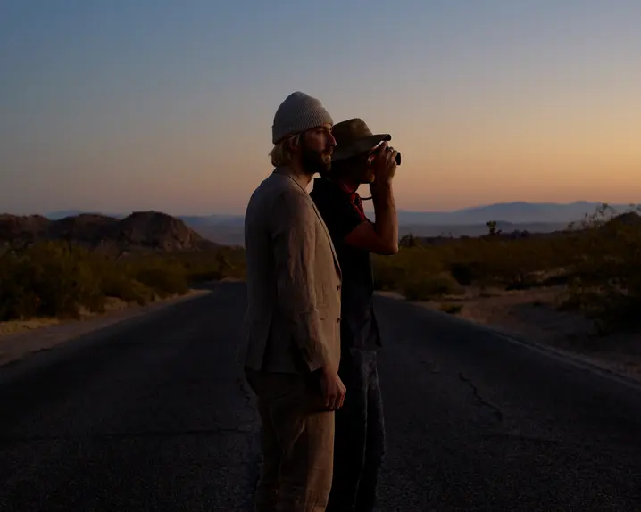 Garrett and Gantry Hill in a desert landscape at sunset, one looking through a camera.