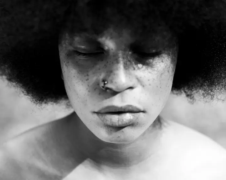 A close-up of a person with closed eyes and Afro hairstyle in black and white
