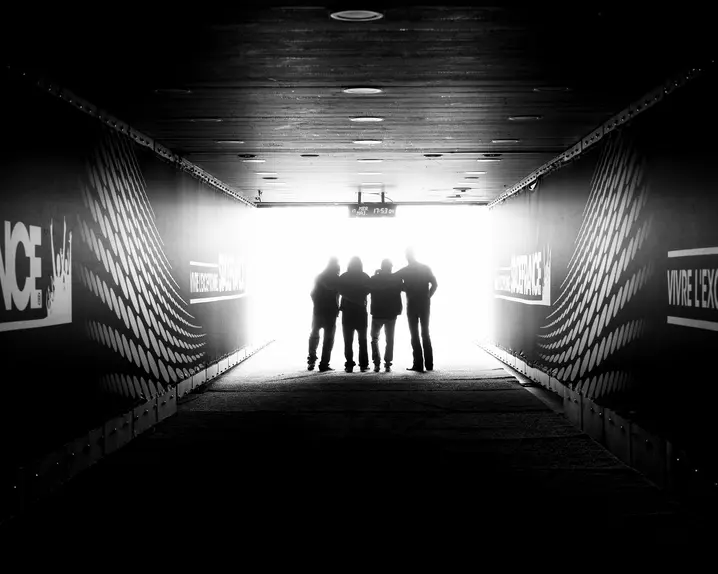 Four people are standing in a stadium tunnel with the sign "Stade France" in the light at the end of the corridor.