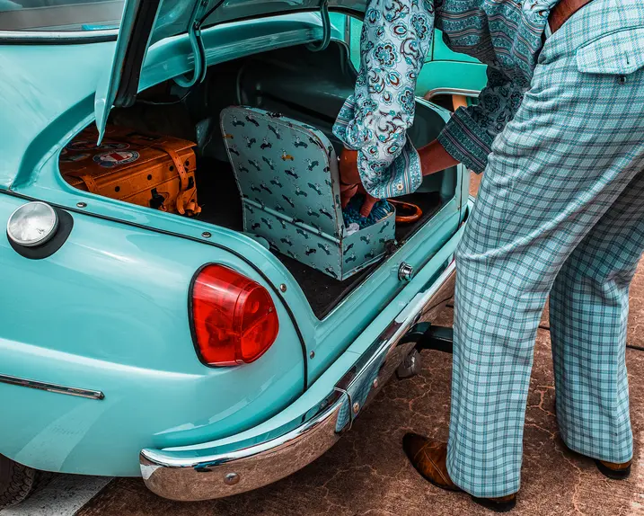 A person packs suitcases into the trunk of a turquoise vintage car.