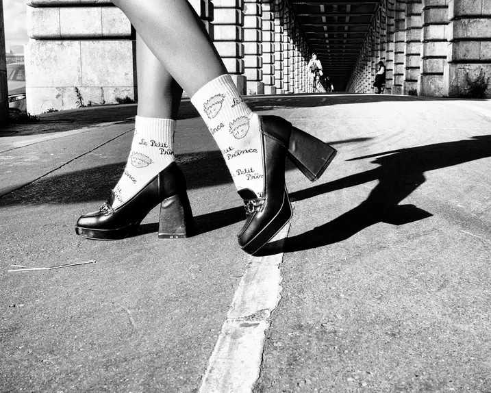 Close-up of legs in high heels on a street under a bridge in black and white.