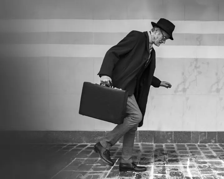 Elderly man in suit with hat and briefcase walking on icy cobblestones.