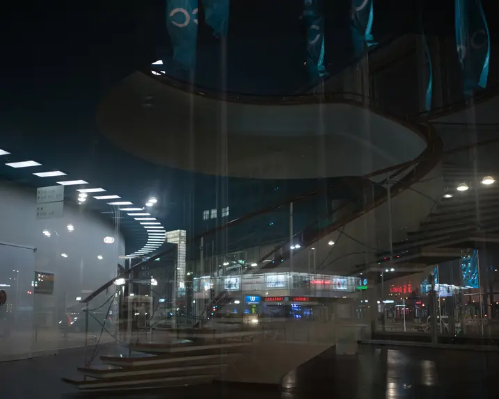 Reflection of a spiral staircase and a city at night in the glass front of a building.