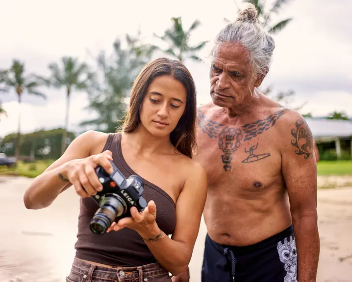 Mainei Kinimaka shows pictures on a camera to a man with Hawaiian tattoos on his upper body