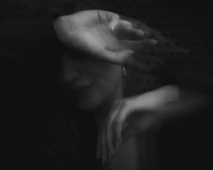 Blurred black and white image of a person covering her face with her arm.
