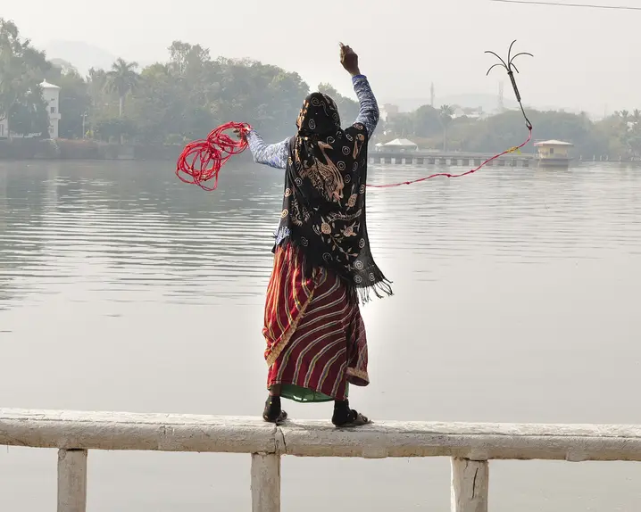 A woman and a child are standing on a railing in front of a lake and are fishing.