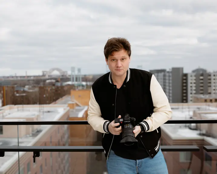 Person holding a camera, in the background are skyscrapers and a bridge on a cloudy day.