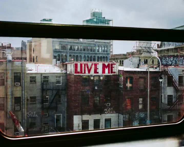 View from a window of a city with a building bearing the graffiti ‘LOVE ME’.