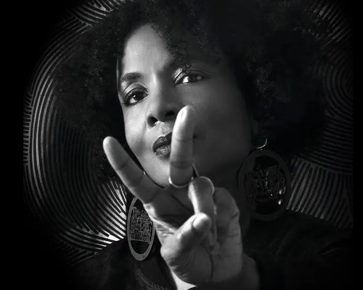 Black and white portrait of a woman with an Afro hairstyle making the peace sign