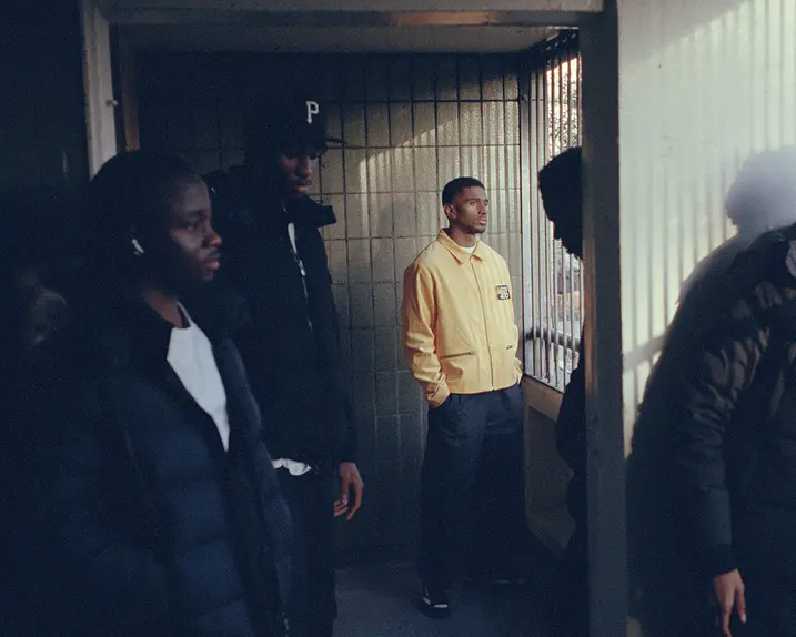 Five men in a shady hallway looking outside, the one in the middle wearing a yellow jacket.