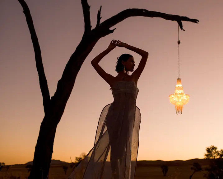 Woman posing under a tree at sunset next to a hanging lantern.