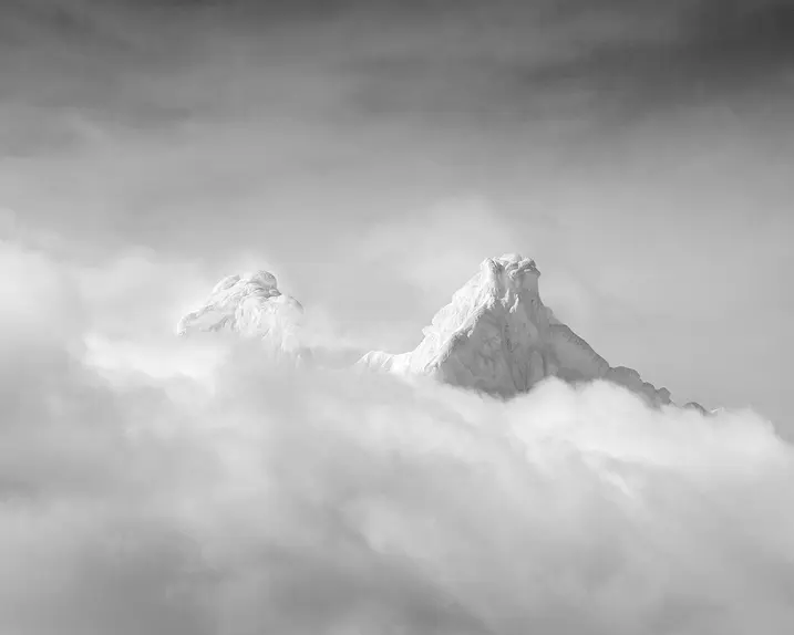 Two snow-covered mountain peaks protrude through a blanket of cloud.