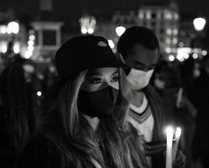 Close-up of a woman and man wearing masks and holding candles in a city at night.