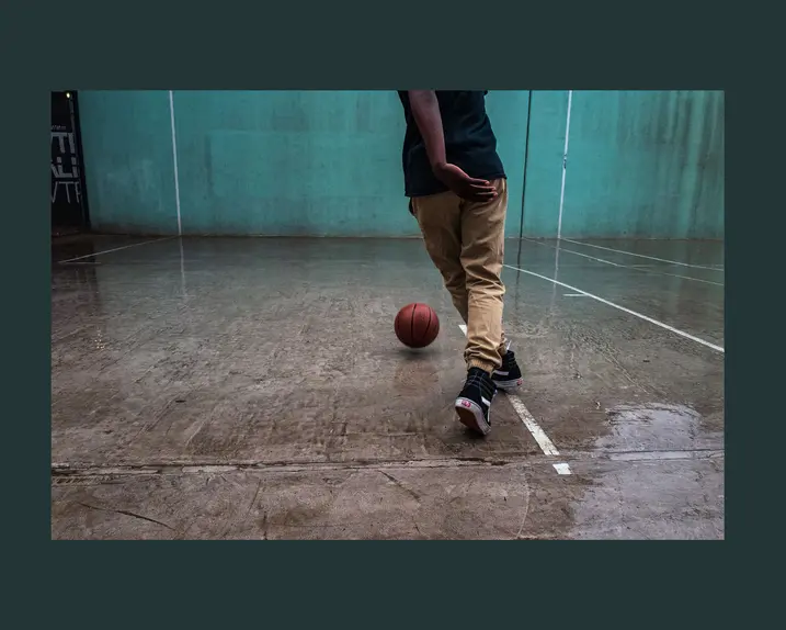 Person playing basketball on a wet court with a turquoise wall in the background.