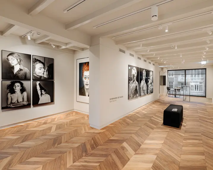 A gallery of Rahi Rezvani's portrait photographs, with the project name Symphony of Faces written on the wall, a light wooden floor and a modern bench.