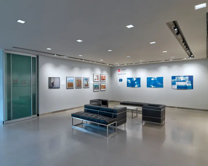 Exhibition room with framed photographs on the wall and black leather armchairs and sofas in the centre of the room.