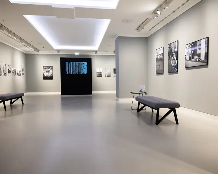 Brightly lit exhibition room with pictures on the wall and benches