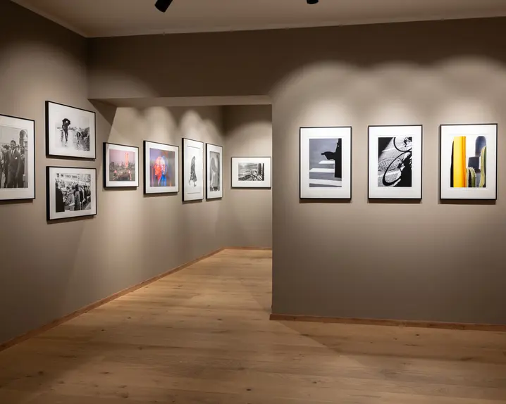 Gallery of black and white and colour photographs on beige walls, discreetly lit and with a light wooden floor.