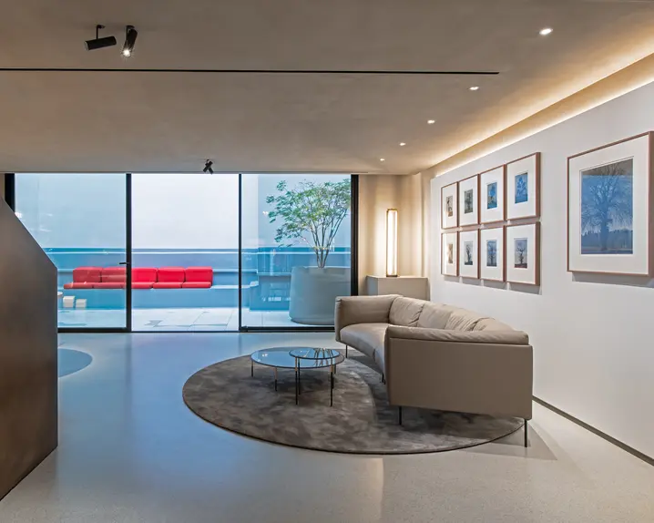 Modern room with sofa, glass table, photographs of trees and view of terrace with red seats.