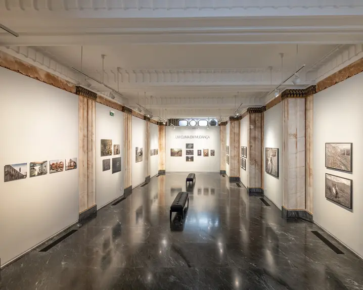 Exhibition room with photographs from different places. At the end of the corridor, on the wall is the writing 'Um clima em mudança', which means 'a changing climate'.