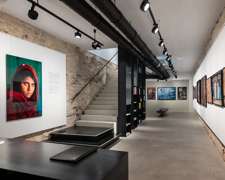 Exhibition room with photographs on the wall and a staircase leading upstairs.