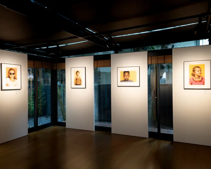 Gallery with four framed portraits of children, exhibited in a modern room with large windows.