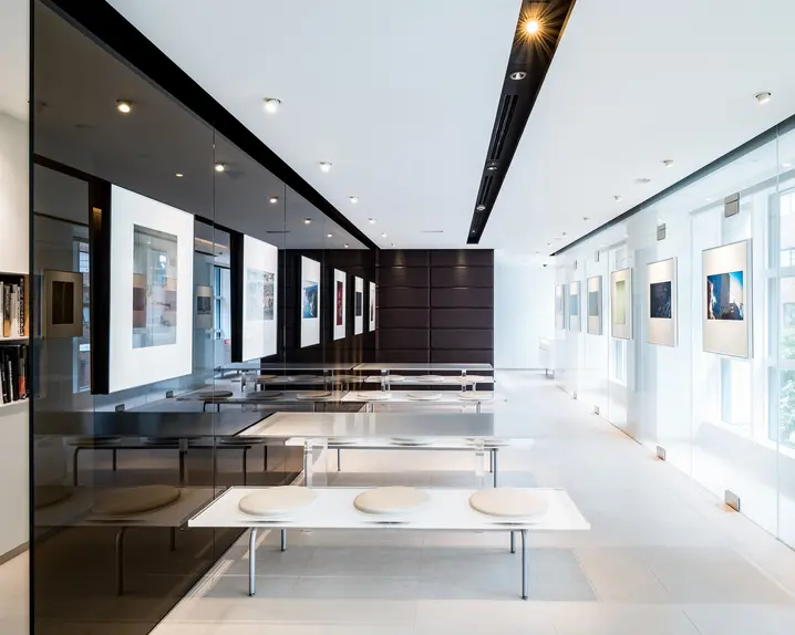 Modern exhibition room with benches and tables, framed photos and glass walls.