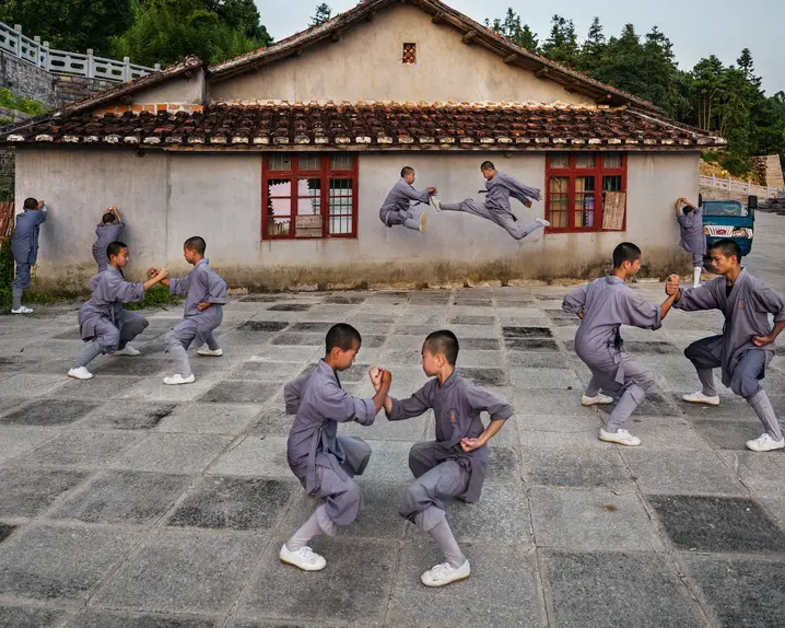 Shaolin monks practise martial arts in the courtyard in front of a traditional building