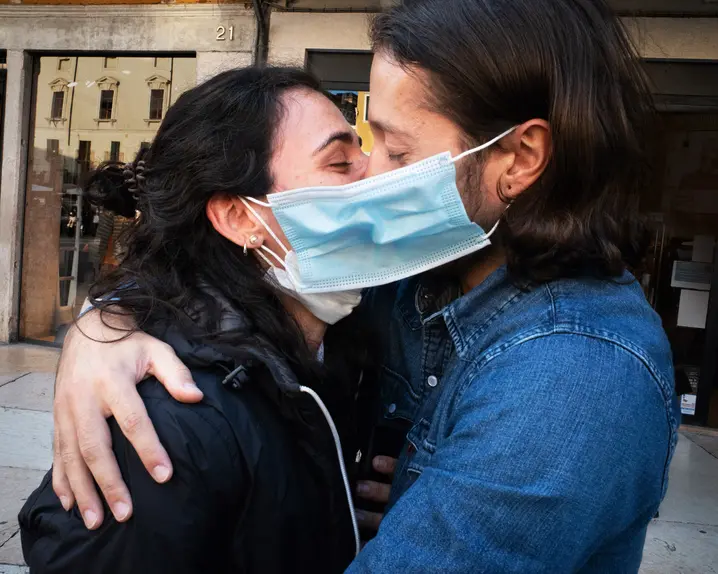 A couple wearing face masks hug and kiss in a street
