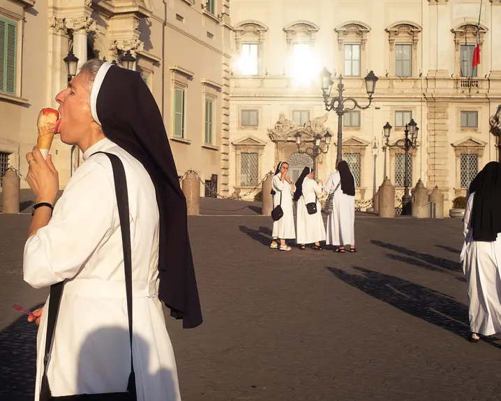 A nun eats an ice cream while several nuns talk in the background.