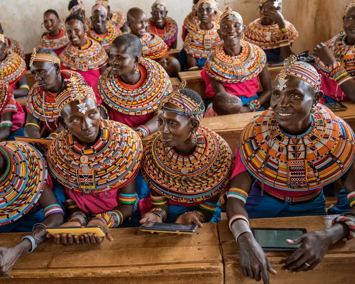 Women from the Samburu tribe in Kenya sitting on a wooden bench in traditional clothes and smiling.
