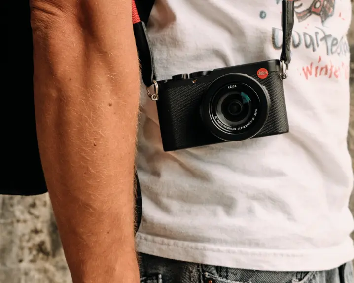 Side shot of a person with a Leica camera hanging in front of his body..