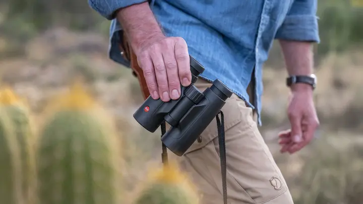 The Leica Trinovid is held in one hand by a man. He carries it casually beside him as he wanders through the landscape