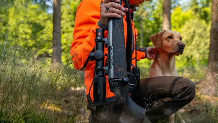The Leica Amplus is the focus of the picture, while a huntress has knelt down and is holding her weapon.