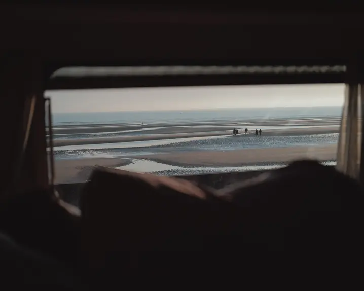 People on the beach photographed from a small window of a caravan