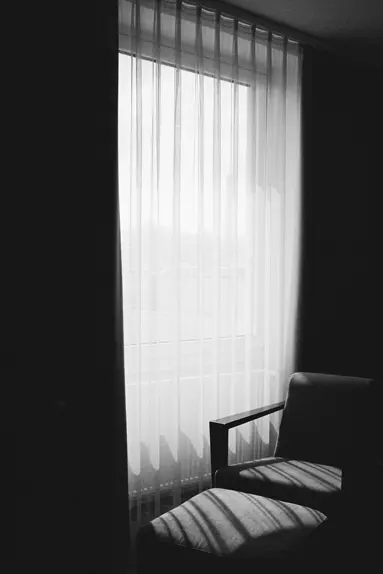 black and white picture white curtains with armchair in front of it