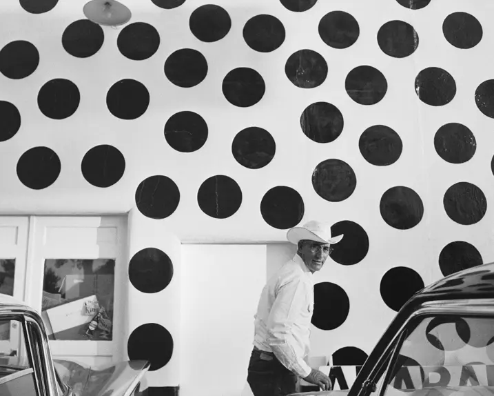 Man with hat in front of a white wall with large black dots