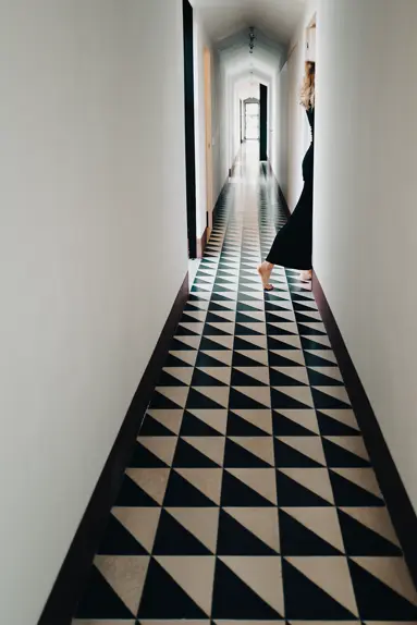long corridor with black and white floor where a woman in a black dress walks through a door